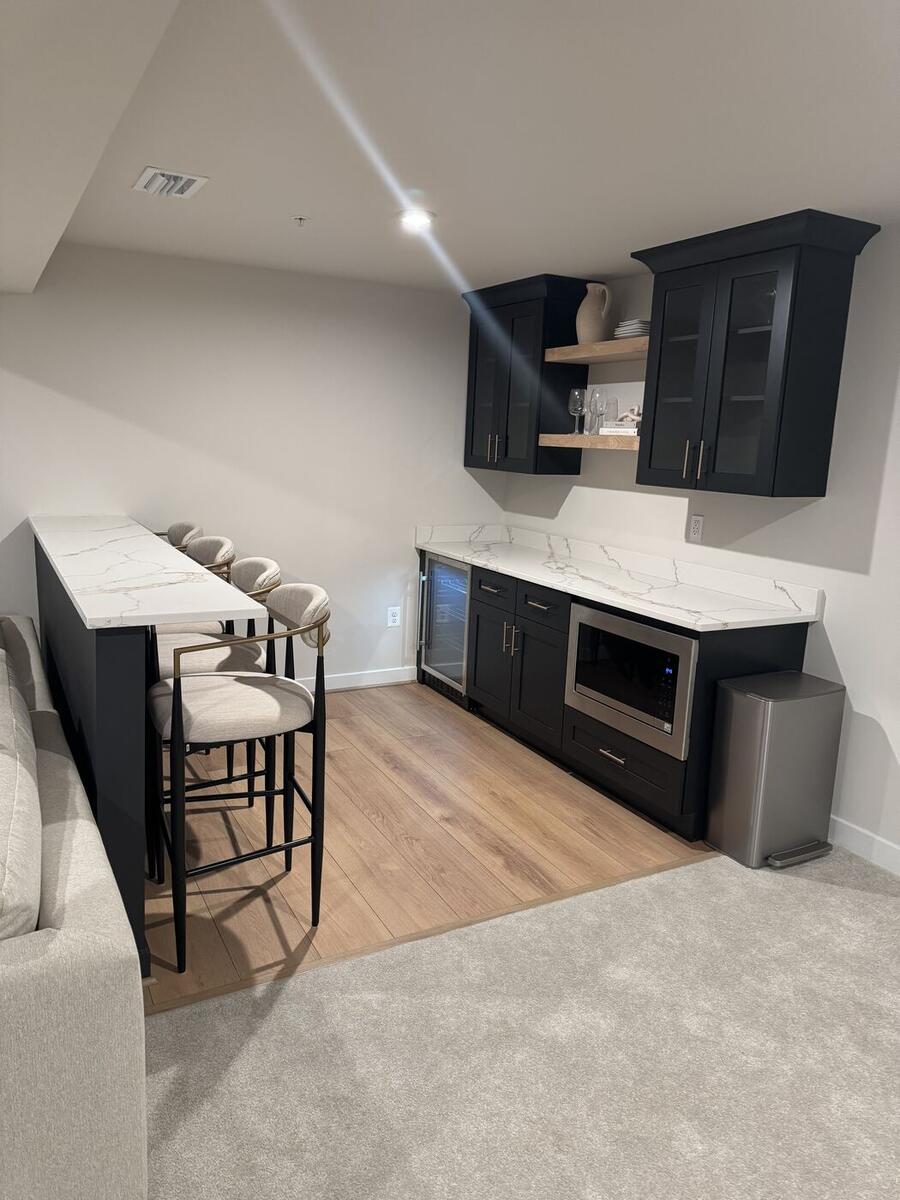 Basement wet bar with island seating, black cabinets and beverage fridge