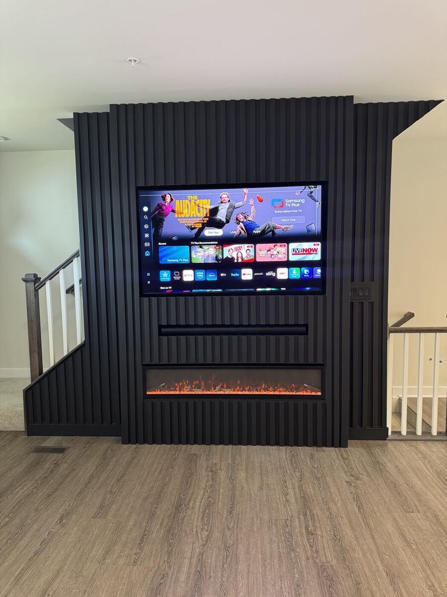 Black slat fireplace wall with TV, built as a room divider in a basement