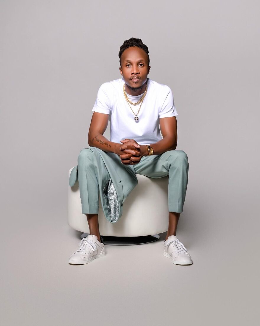 Derrick Adepegba, owner of Dazzu Remodeling, seated in a white t-shirt and sage suit trousers
