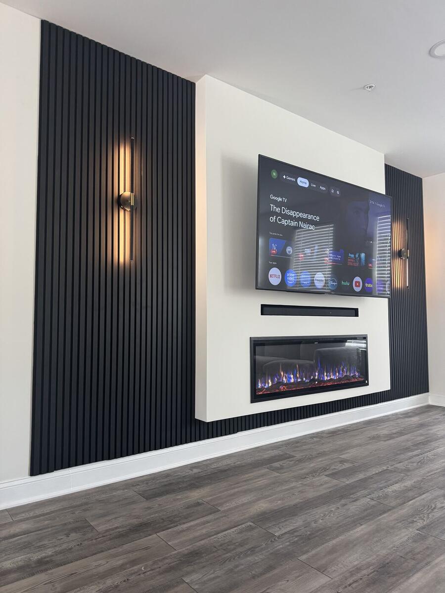 Black fluted panel with sconces beside a white fireplace section and TV